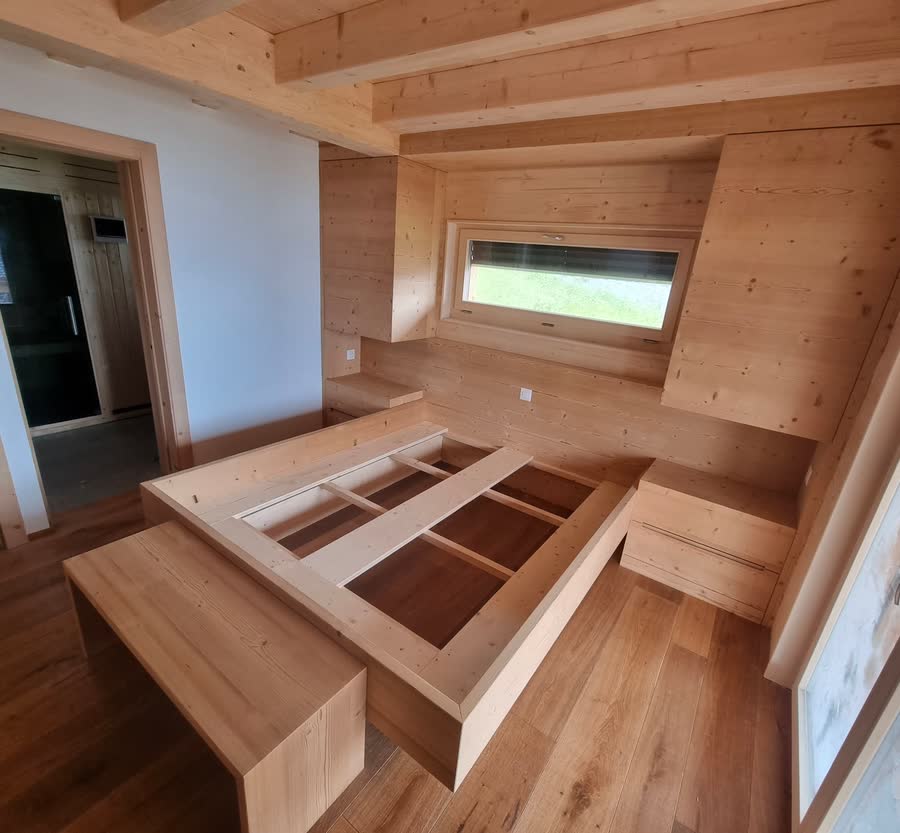 Chambre de chalet contemporaine : structure de lit sur-mesure en bois massif, chevets et banc intégrés, lambris mural et plafond à poutres apparentes.